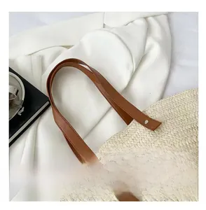 Close-up of woven straw bag with brown leather strap and metal rivet reinforcement