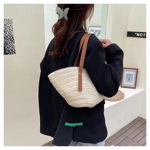 Detail of a large woven straw tote bag with brown straps worn by a model in a modern room