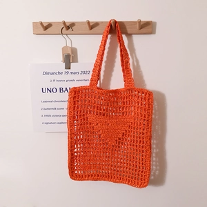 Handmade orange crochet straw tote bag with hollow mesh design hanging on a wooden hook