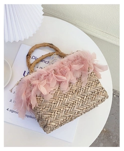 Detail of handmade straw bag featuring pink feathers and bamboo handles for beach vacations