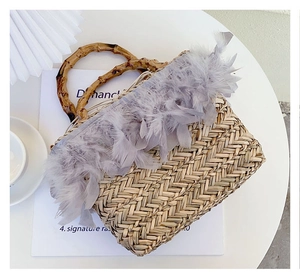 Detail of hand-woven straw bag featuring grey feather trim and natural bamboo handles