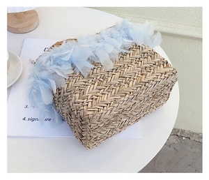 Detail of straw woven bag with light blue feather trim on a white decorative table