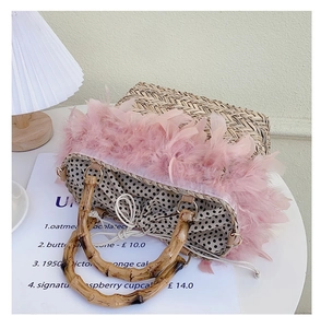 Close-up of woven straw bag featuring pink feather trim and natural bamboo handles