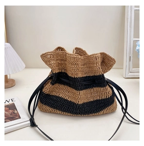 Detail of striped woven straw bucket bag with black leather drawstring and strap