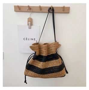 Detail of striped handmade straw bucket bag with black drawstring closure and leather strap