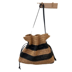 Handwoven striped straw bucket bag with black leather shoulder strap and drawstring closure
