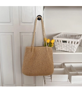 Détail d'un sac cabas en paille tissé à la main avec tulipes jaunes suspendu à une porte