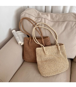 Gros plan de sacs à bandoulière en paille tressée beige et marron sur un canapé