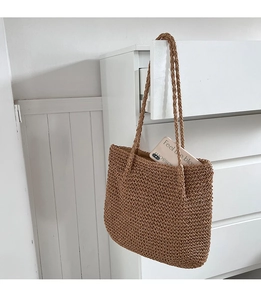 Détail d'un sac cabas en paille tissé à la main accroché sur un tiroir blanc