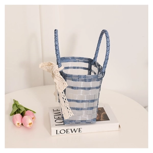 Detail of woven jelly basket bag featuring blue straps and a delicate lace bow accent