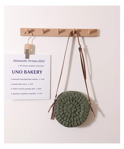 Detail of round woven straw crossbody bag in forest green with a brown leather strap