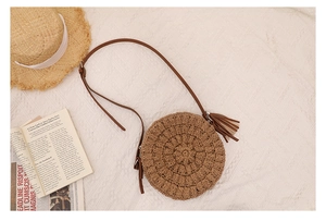 Top view of a round straw crossbody bag with tassel and adjustable brown leather strap