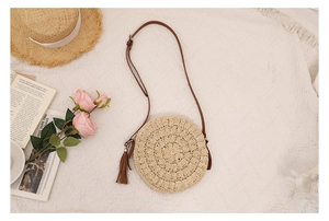 Detail of round straw crossbody bag with brown tassel and adjustable leather strap