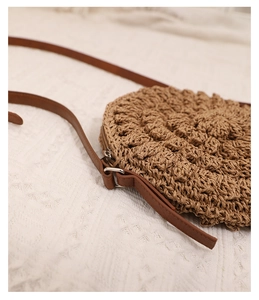 Close-up of a circular hand-woven straw crossbody bag with wavy texture and leather strap