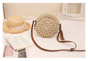 Detail of round straw crossbody bag featuring textured weave and brown tassel accent