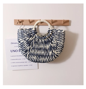 Detail of navy and beige woven straw handbag with circular handle on a wooden hook