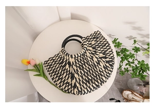 Detail of half-moon straw handbag with two-tone black and beige woven pattern handles