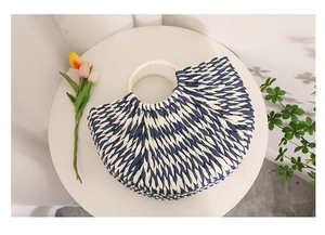 Detail of blue and white striped woven straw bag with round cream handle and semicircular shape