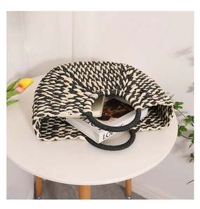 Detail of semicircular straw tote with black and white geometric weave on a white table