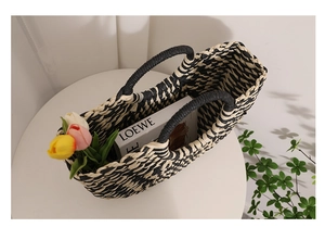 Close-up of woven tote bag with black chevron pattern holding tulips and books