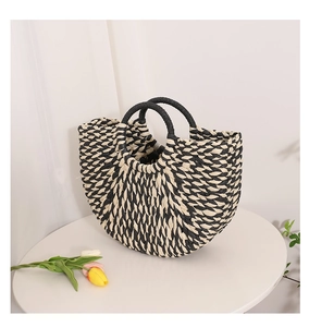 Detail of a semi-circular woven straw handbag with black and white rope patterns
