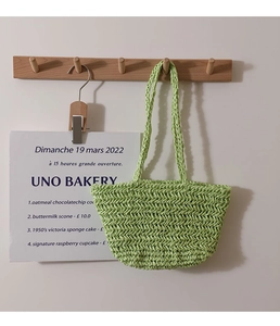 Detailed view of green woven straw bag featuring herringbone pattern on wooden wall hook