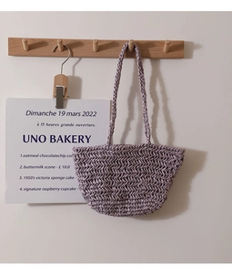 Detail of lavender straw woven tote bag hanging on wooden hook with French poster backdrop