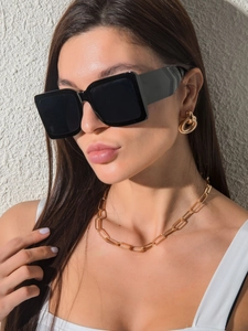 Close-up of square black sunglasses paired with gold chunky hoop earrings and paperclip necklace