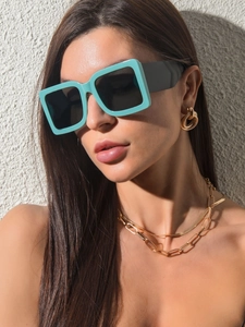 Detail of square mint green sunglasses featuring wide frames and dark lenses on a model