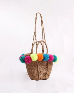 Handmade straw bucket bag with colorful pom-pom trim and dual handles for beach vacation