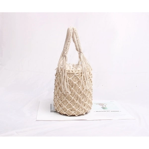 Détail d'un sac seau beige tissé à la main avec filet et poignée décorative à glands