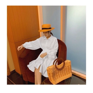 Detail of a large striped straw beach bag on a table with a white shirt dress