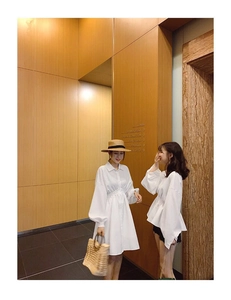Lifestyle shot of a woven straw beach bag paired with a white puff sleeve summer dress