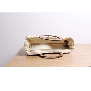 Detail of straw beach bag showing the wooden handles and secure zipper closure system