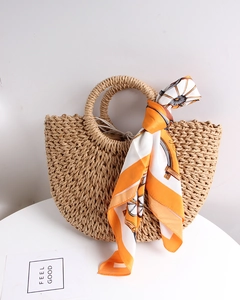 Close-up of semi-circular straw bag with woven handles and geometric silk scarf detail