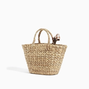 Handmade straw beach bag with woven handles and brown checkered bow on white background