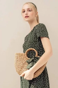 Detail of a semi-circular straw handbag with a green polka dot silk scarf on the handle