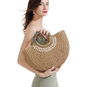 Detail of half-moon straw bag featuring shell embellishments and woven circular handle
