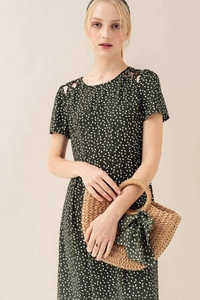 Detail of round straw bag with decorative bow and woven handle against beige backdrop