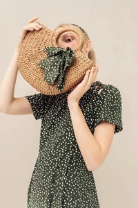 Detail of handmade straw woven handbag with green polka dot ribbon and circular handle