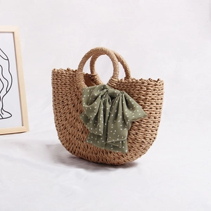 Handcrafted semicircular straw tote bag with green polka dot bow on the round handle