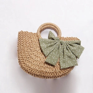 Handmade woven straw handbag with a green polka dot bow and round handles in brown