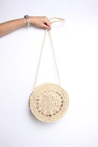 Detailed close-up of woven hollow flower pattern on beige round straw beach shoulder bag