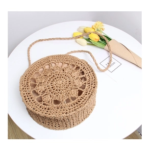 Detail of hand-woven straw bag with hollow floral pattern and shoulder strap on table