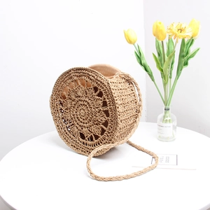 Detail of hand-woven round straw bag featuring floral hollow pattern and woven strap
