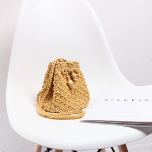 Detail of handmade knit crossbody bucket bag with drawstring and wooden beads on a white chair
