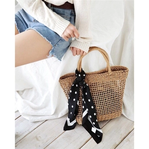 Detail of straw woven tote bag featuring cutout hollow design and polka dot silk scarf handle