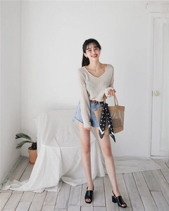 Detail of light beige V-neck knitted sweater paired with straw bag and denim shorts