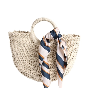 Handmade half-moon straw beach bag with decorative striped silk scarf on handles