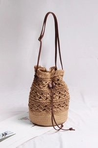 Close-up of woven straw bucket bag with hollow mesh pattern and leather drawstring closure